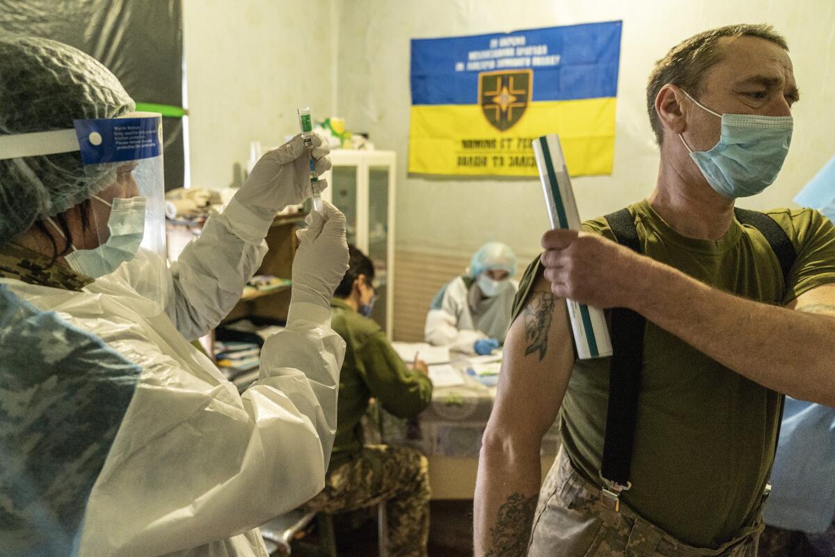 A Ukrainian serviceman prepares to receive a dose of the AstraZeneca COVID-19 vaccine marketed under the name CoviShield at a military base near the front-line town of Krasnohorivka, eastern Ukraine, Friday, March 5, 2021. The country designated 14,000 doses of its first vaccine shipment for the military, especially those fighting Russia-backed separatists in the east. But only 1,030 troops have been vaccinated thus far. In the front-line town of Krasnohorivka, soldiers widely refuse to vaccinate. (AP Photo/Evgeniy Maloletka)