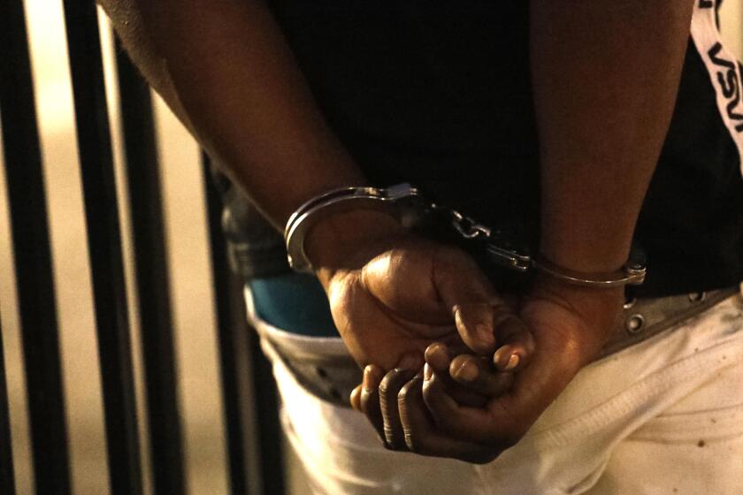 LOS ANGELES, CA - JULY 25, 2019 - - A man is detained and placed in handcuffs while Los Angeles police officers search the car he was riding in with other youths in South Los Angeles on July 25, 2019. Officers found a gun and bullets on the floor of the vehicle. One of the youths was arrested for illegal possession of a firearm. (Genaro Molina / Los Angeles Times)