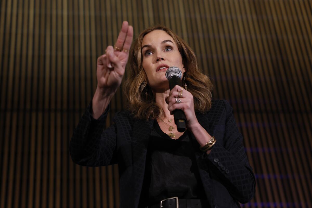 A woman holds up two fingers on one hand while holding a microphone with her other hand. 