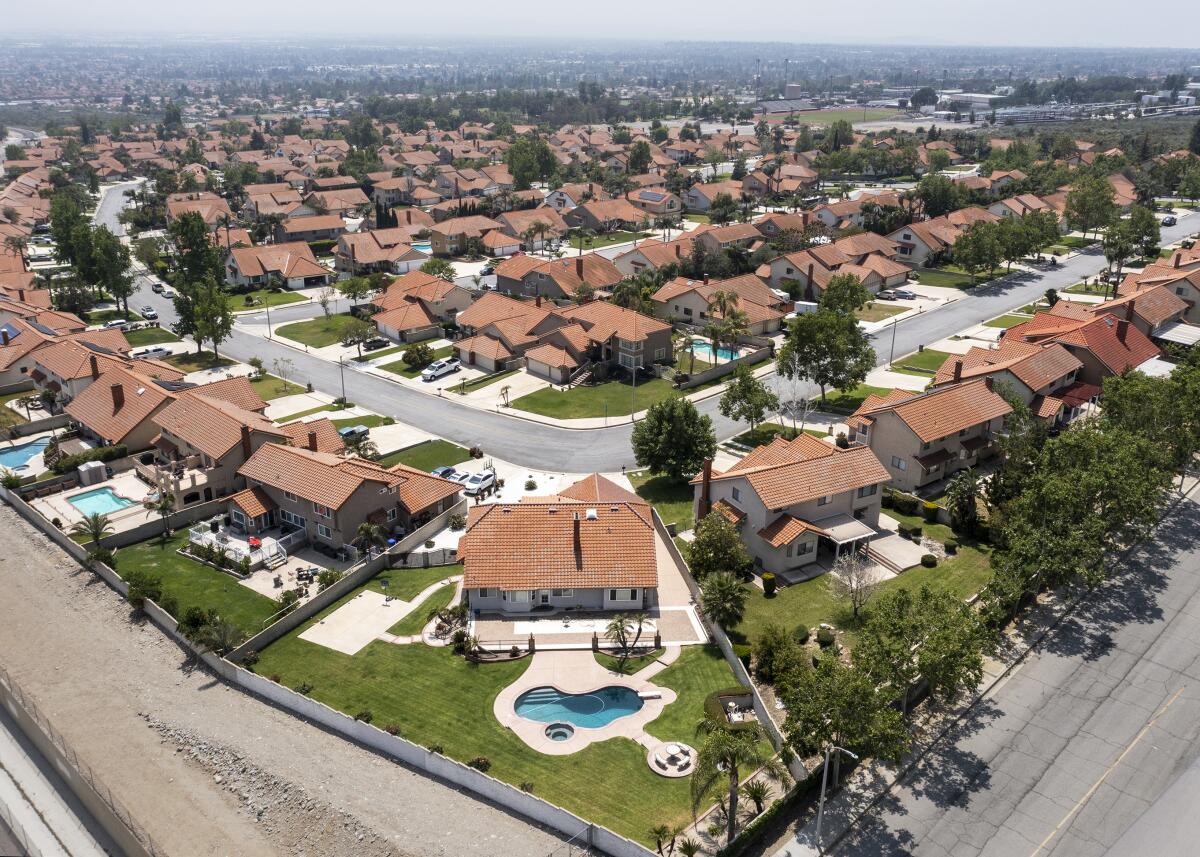 An aerial view of of a single-home suburban neighborhood. Several homes have a pool and all have grass lawns.