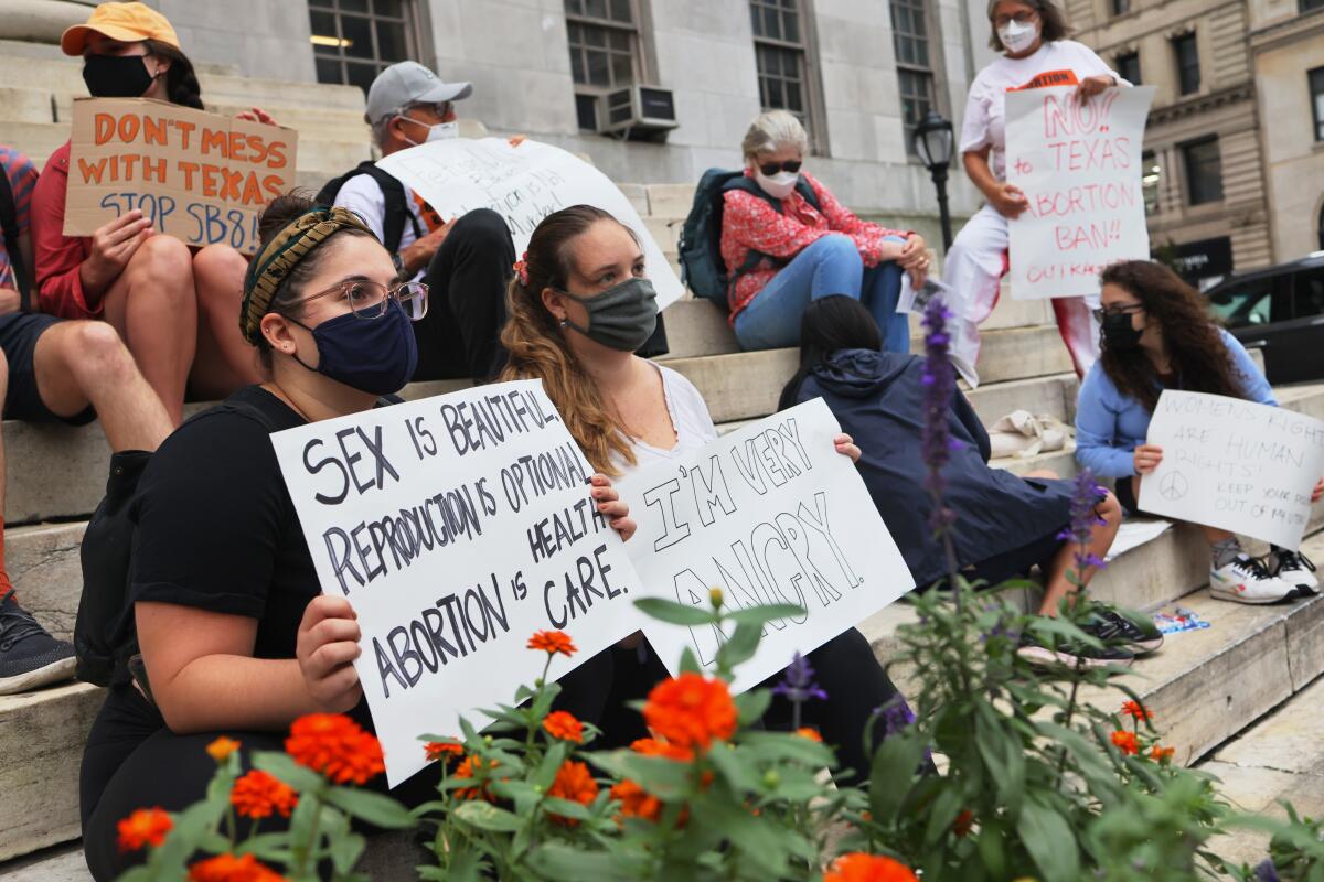A group of women sit on steps wearing masks and holding reproductive rights signs. 