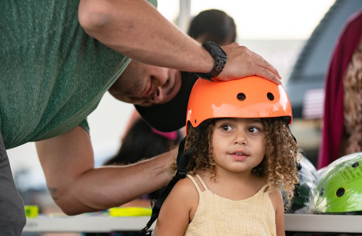 Joelle's father straps a helmet onto her head at the Huntington Beach Police Department's Bike Rodeo.