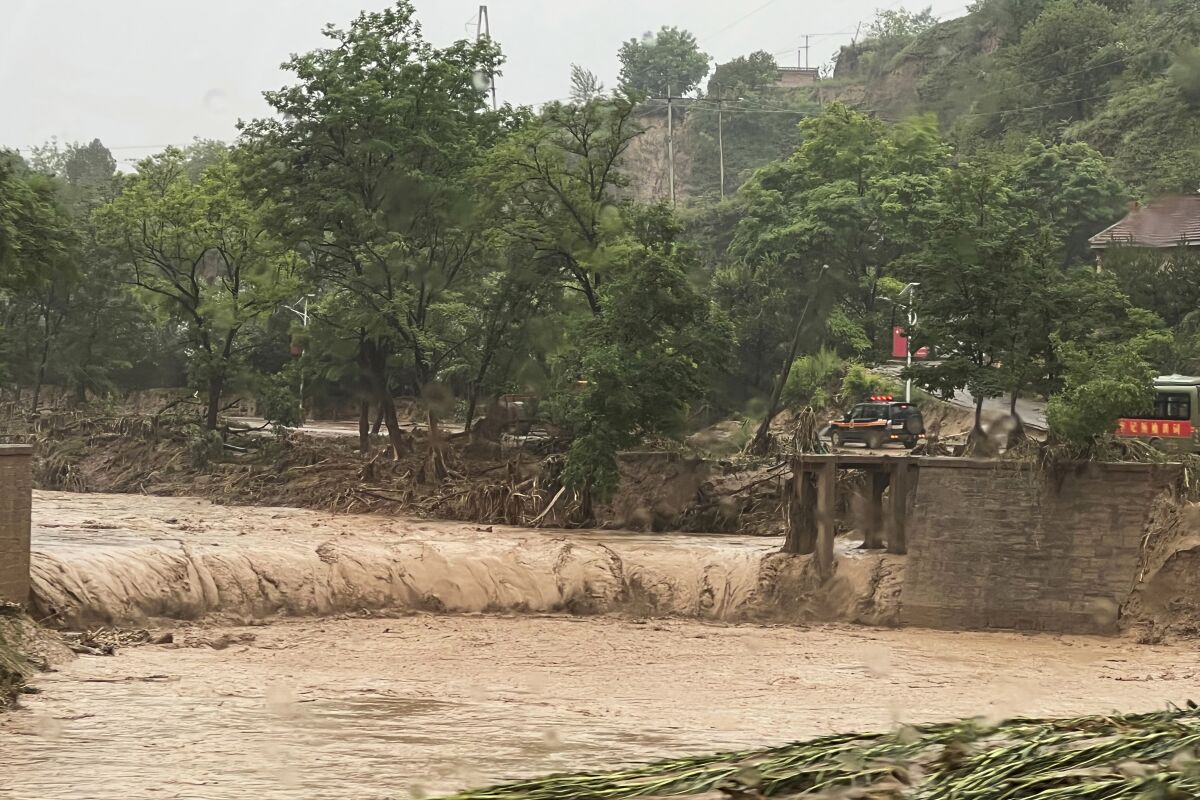 A vehicle is seen near a part of a bridge that was washed away by flood waters along a river in Qingyang in northwest China's Gansu province Saturday, July 16, 2022. Flash floods in southwest and northwest China have left at least a dozen dead and put thousands of others in harm's way, state media reported Sunday. (Chinatopix Via AP)