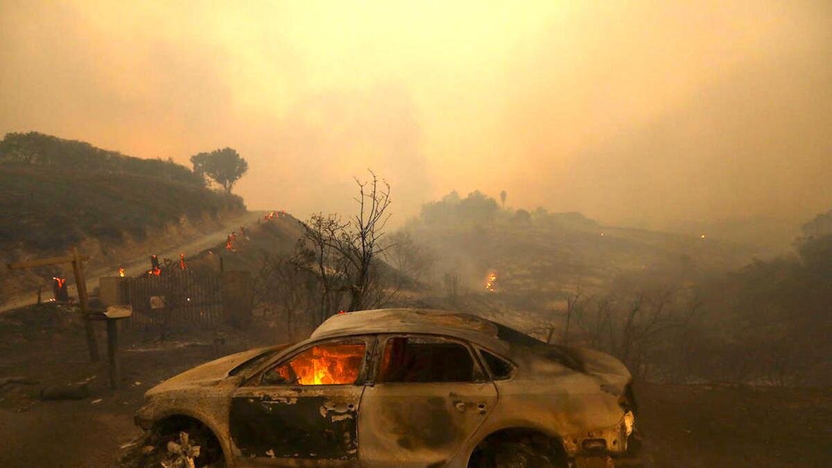Un automóvil carbonizado todavía arde como otra víctima del fuego de Woolsey contra una ladera carbonizada en Malibú.