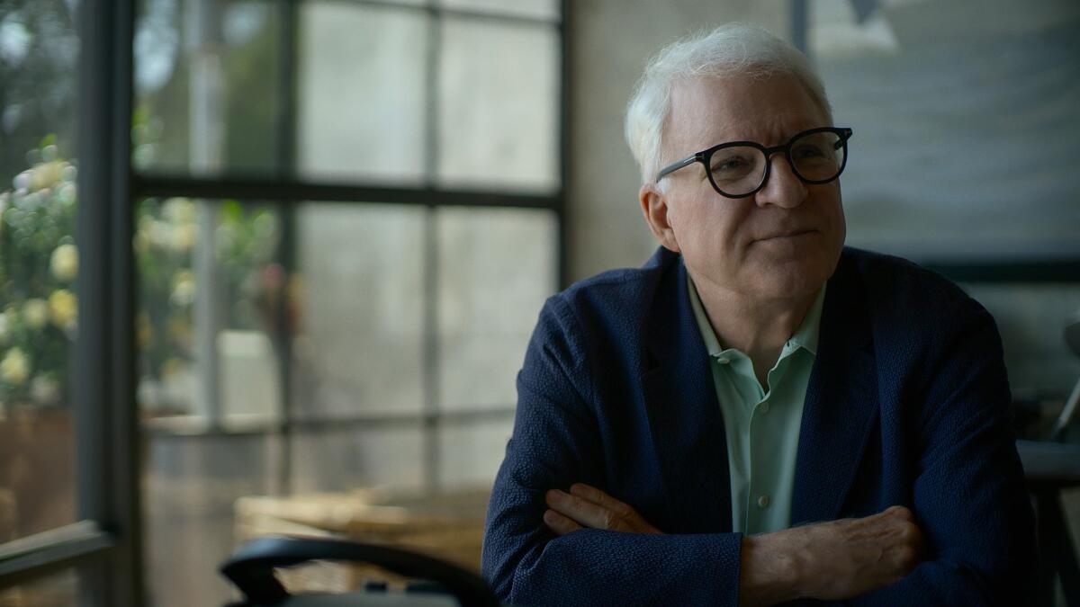 Steve Martin sits at a table.
