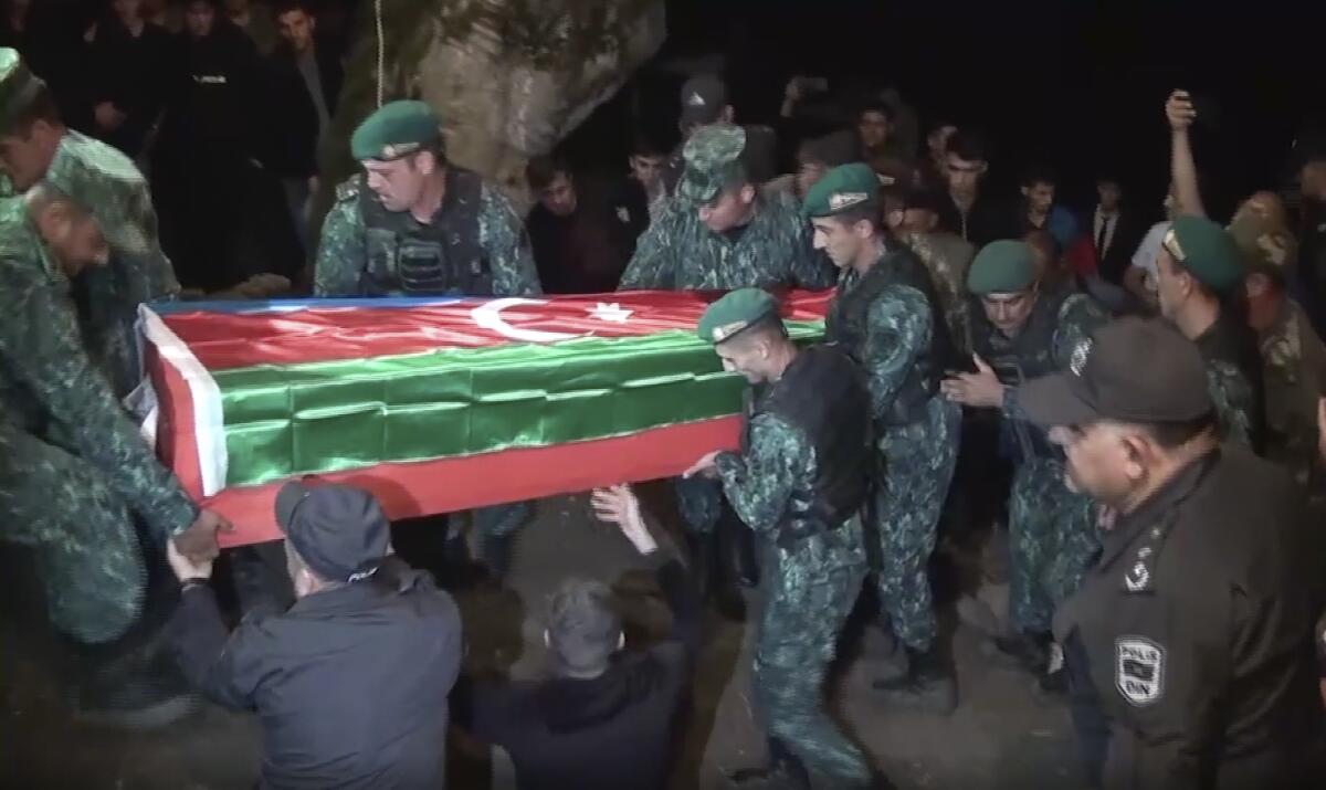 Troops in fatigues and berets carrying a flag-draped coffin