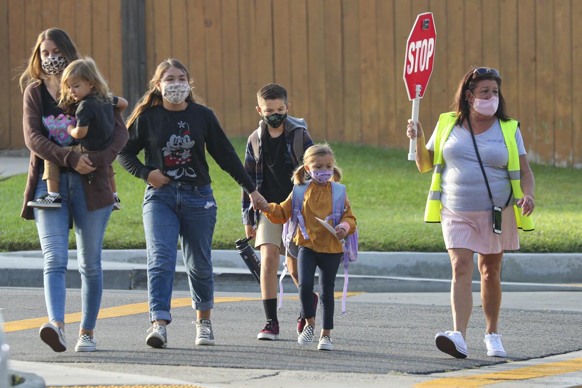 A crossing guard leads students and parents across a street