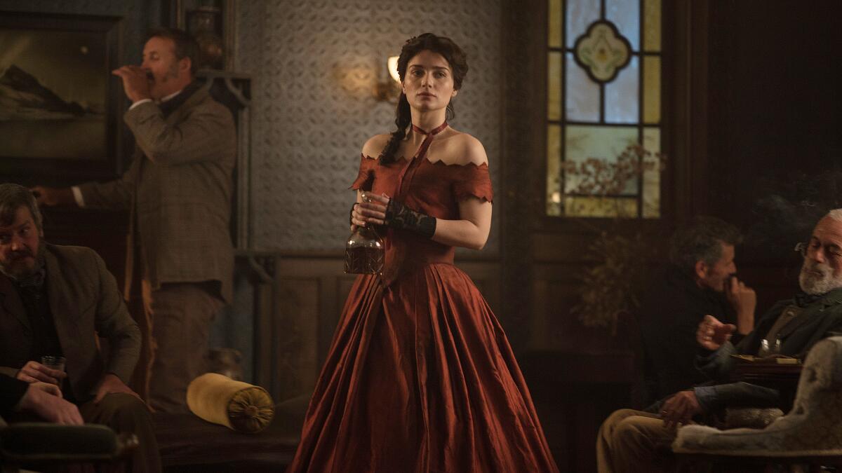 "The Luminaries" actress Eve Hewson in a flowing red dress, with a stained glass window behind her.