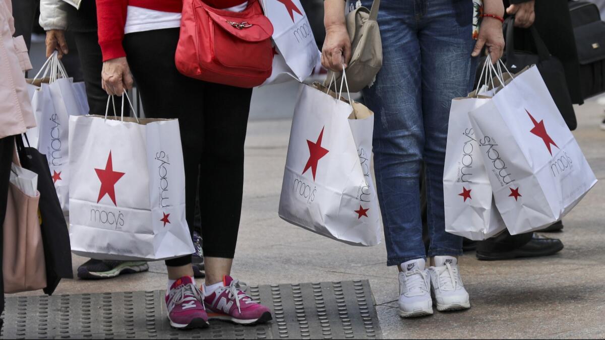 Shoppers holding bags from Macy's wait to cross an intersection in New York.