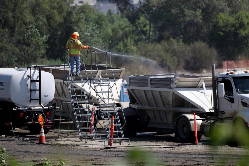 A worker hoses down a truck as it heads out with a load of dirt from the Hahamongna Watershed Park L.A. County Public Works Department's Devil's Gate Dam Sediment Removal project, in La Canada Flintridge on Tuesday, July 30, 2019.