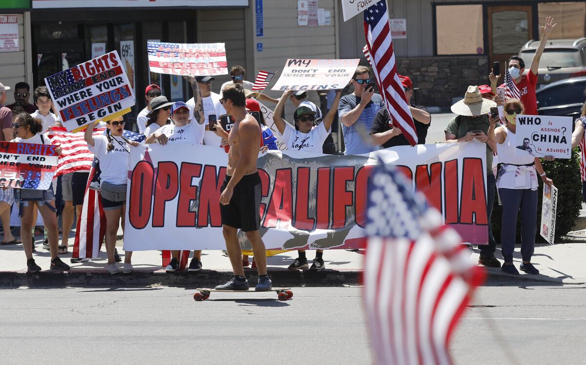 A skateboarder films protesters Sunday along Mission Boulevard in Pacific Beach during a rally demanding the reopening of California.