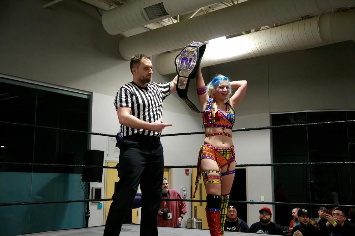 A referee points to a female wrestler and holds her hand up in victory.