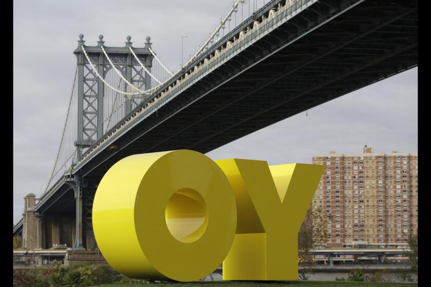The Manhattan Bridge frames a bright yellow monumental sculpture by artist Deborah Kass in Brooklyn Bridge Park, on Wednesday, Nov. 11, 2015, in New York. When viewed from Manhattan, the sculpture reads "Yo," but when viewed from Brooklyn it spells the popular Yiddish expression "Oy." The aluminum sculpture was commissioned by Brooklyn developer Two Trees Management Company and will remain up until August 2016.