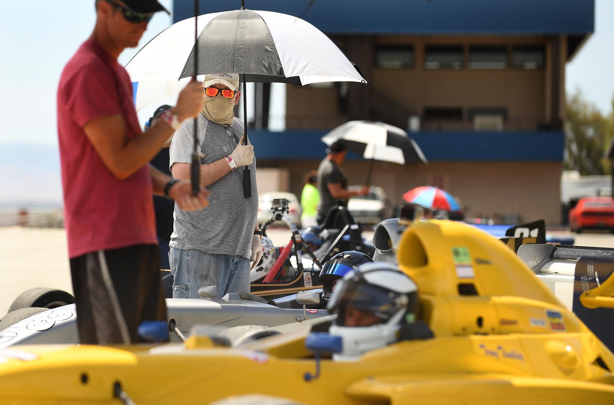 Race car team members help keep shade on their drivers before a race at Buttonwillow Raceway in Buttonwillow, Calif., on Saturday.