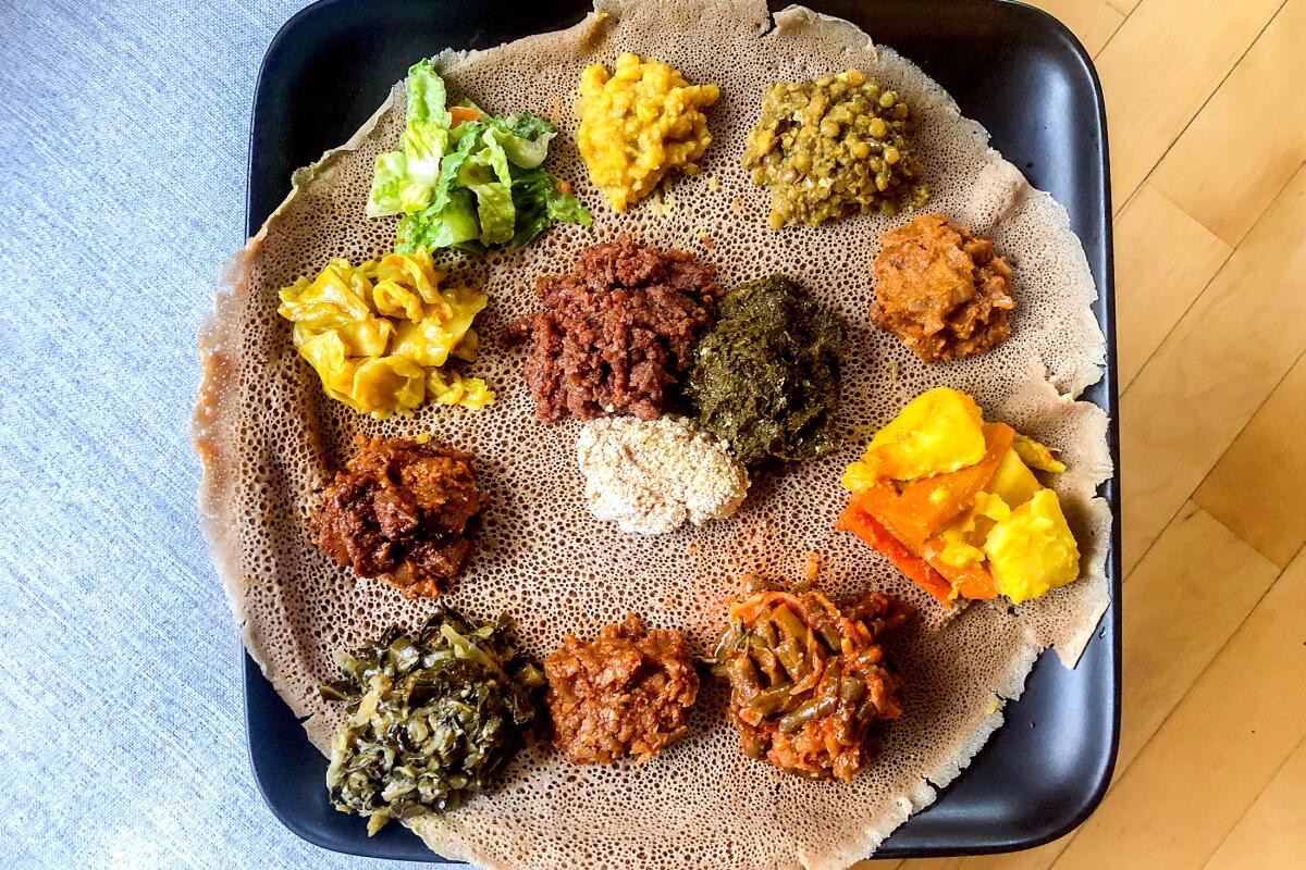 Colorful dollops of vegetarian stews on a round injera bread on a square plate
