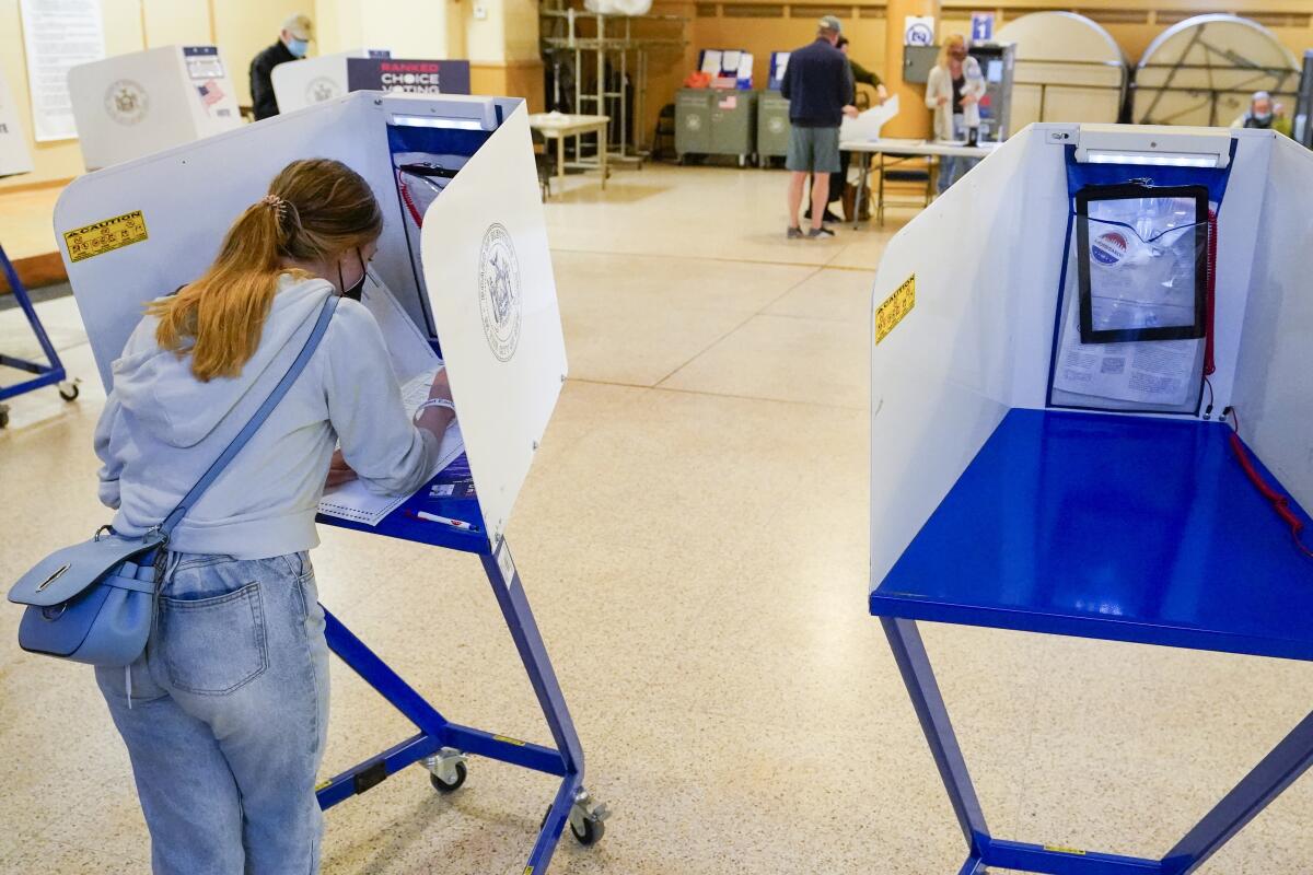 A woman marks her ballot in a voting booth in a room of spaced-out voting booths