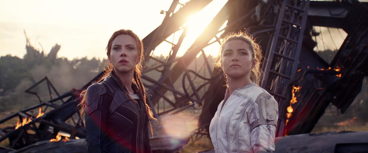 Scarlett Johansson as Black Widow/Natasha Romanoff and Florence Pugh as Yelena Belova stand in front of ruins on fire
