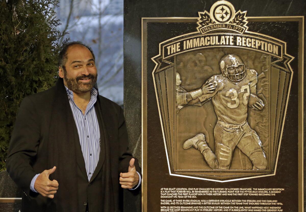Franco Harris gives two thumbs up next to a plaque.