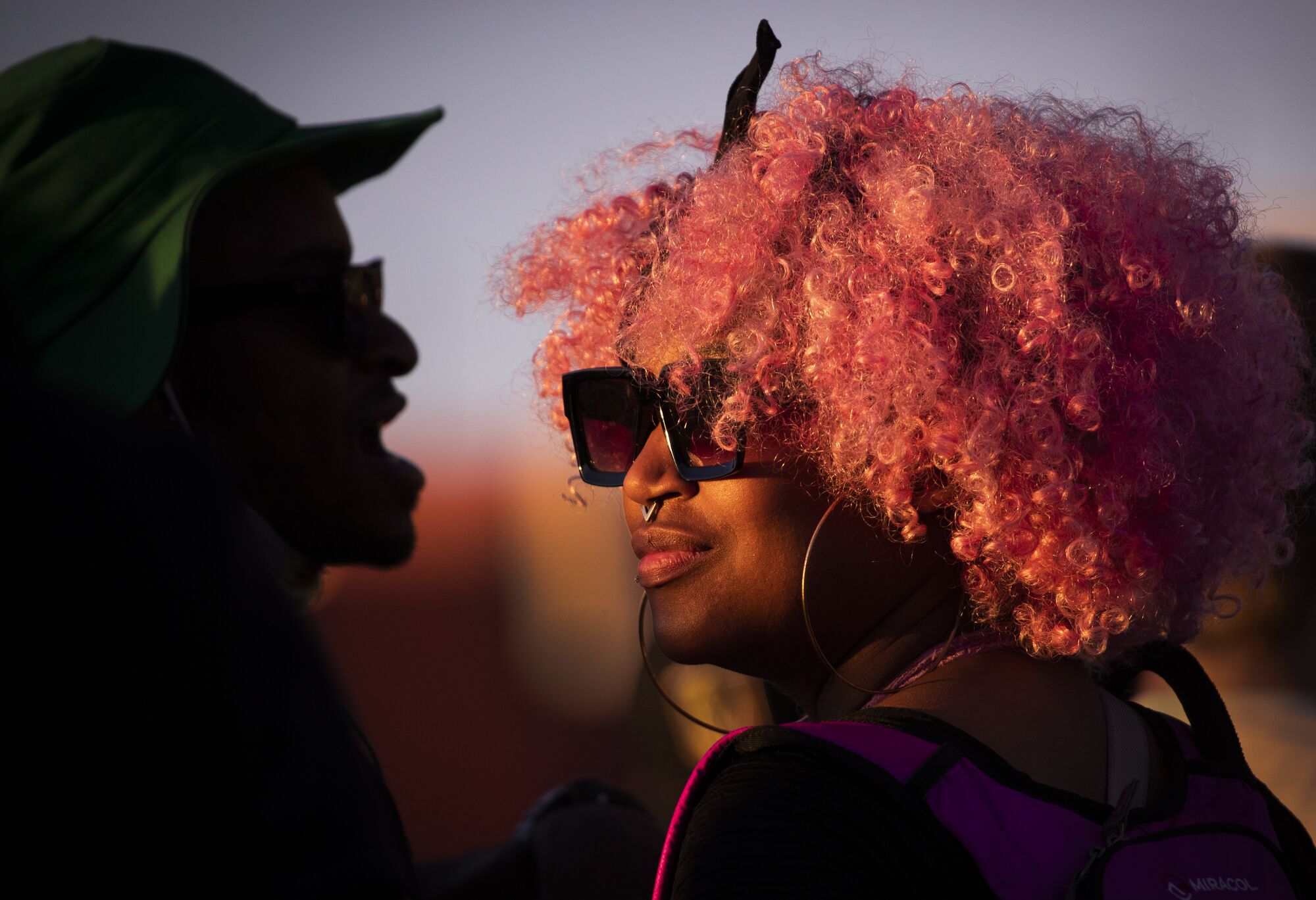 A woman with sunglasses, a pink afro and a septum piercing, right, and a silhouette of a man