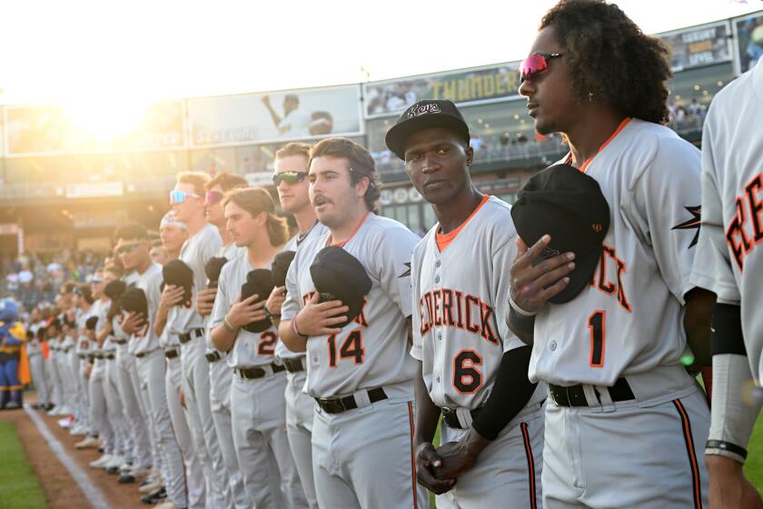 Trenton, New Jersey June 2, 2023-Not understanding the etiquette of the National Anthem, Frederick Keys player Dennis Kasumba looks to teammates for guidance before a game with the Trenton Thunder in Trenton, New Jersey. (Wally Skalij/Los Angeles Times)