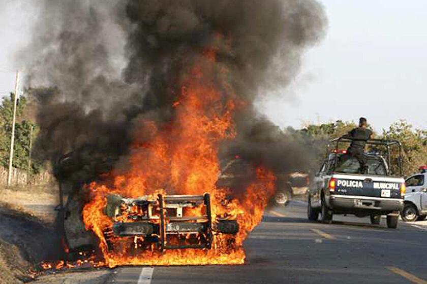 Police officers drive past a burning police vehicle in Zihuatanejo, Mexico. In a three-week period, five grenade attacks were launched on police patrols and stations.