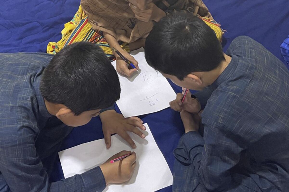Three children in Afghanistan use pens and paper on a floor