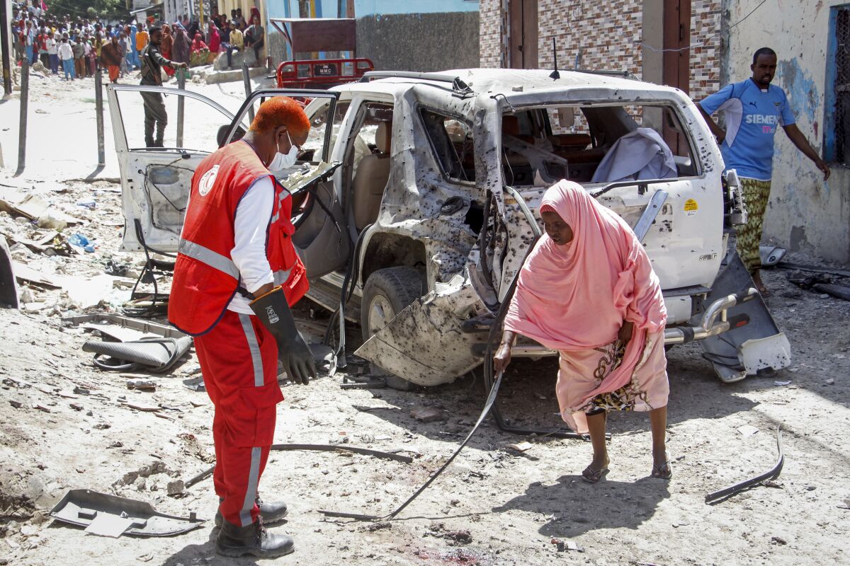 A woman, right, points a medical worker to remains of the suicide bomber at the scene, after Somalia's government spokesperson Mohamed Ibrahim Moalimuu was wounded in a suicide bombing in Mogadishu, Somalia, Sunday, Jan. 16, 2022. Moalimuu appeared to be the sole target of the attack near his residence by a busy intersection in the capital, for which the al-Shabab extremist group has claimed responsibility. (AP Photo/Farah Abdi Warsameh)