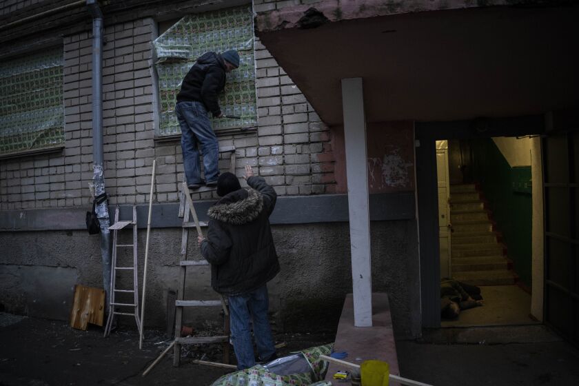 Two residents use food-packaging material to cover windows of a damaged building during a recent Russian strike while another resident lies inebriated at the entrance of a building in the southern city of Kherson, Ukraine, Sunday, Nov. 27, 2022. Shelling by Russian forces struck several areas in eastern and southern Ukraine overnight as utility crews continued a scramble to restore power, water and heating following widespread strikes in recent weeks, officials said Sunday. (AP Photo/Bernat Armangue)