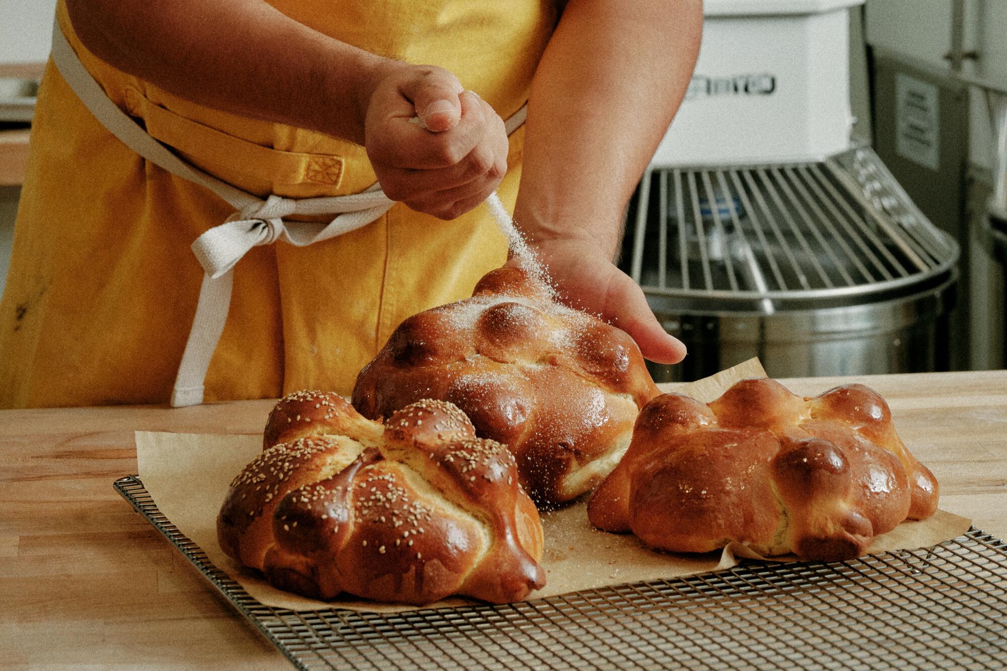 Gusto Bread owner Arturo Enciso sprinkles sugar onto pan de muerto after he brushed the buns with melted butter.