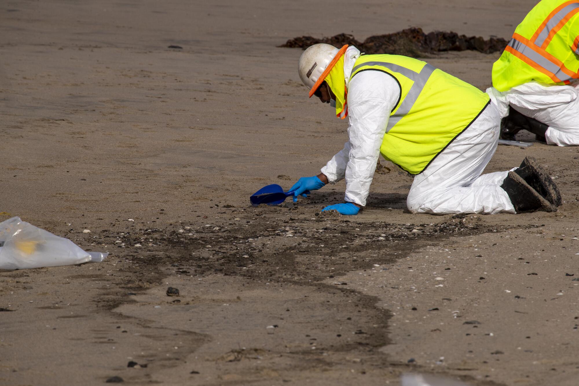 Workers scrape up oily sand for removal.  