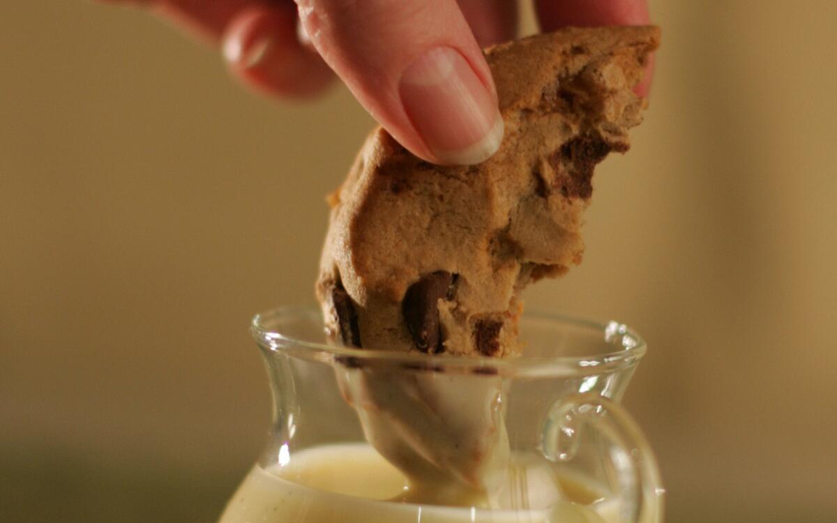 Half a chocolate chip cookie being dunked in milk
