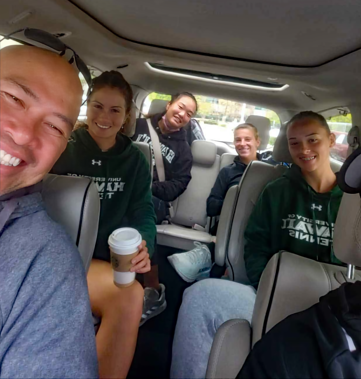 Hawaii women's tennis coach Jun Hernandez sits in a car with players during a road trip last year.