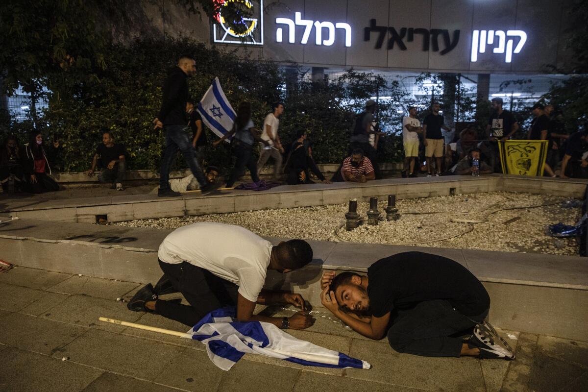 People, some bearing Israeli flags, stay low to the ground while others mill about during a rocket attack
