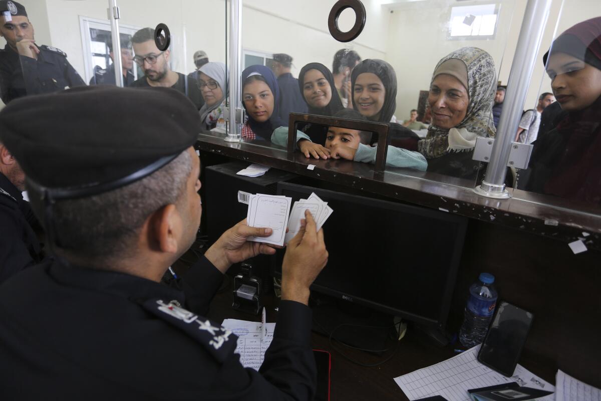 A border agent at a desk looks at papers as Palestinians with dual nationality stand on the other side of a clear barrier. 