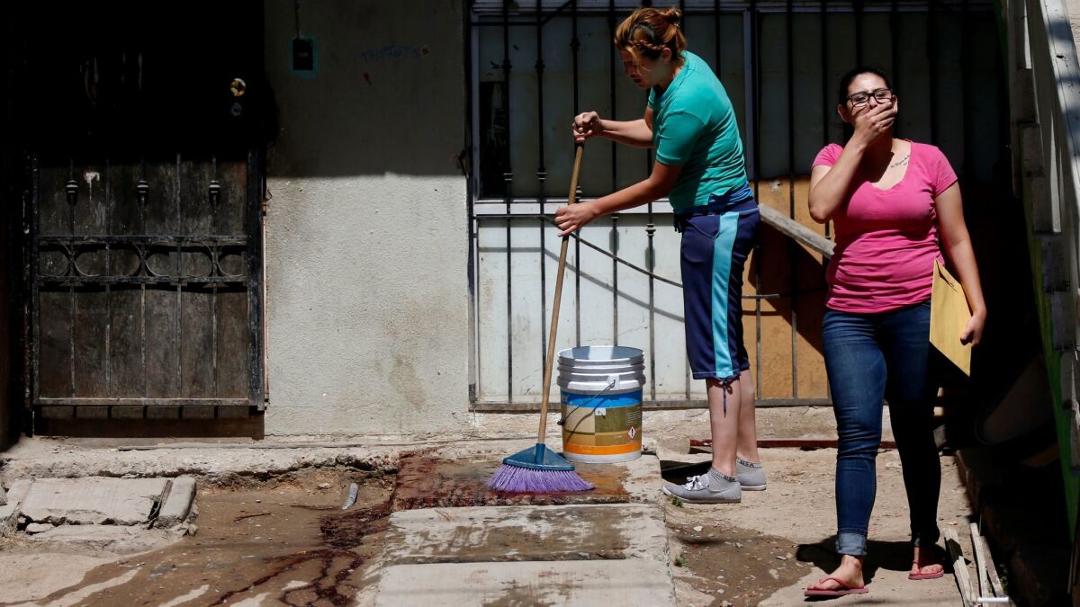 A Tijuana woman washes blood from in front of her house, where her husband was shot and killed in broad daylight in April.