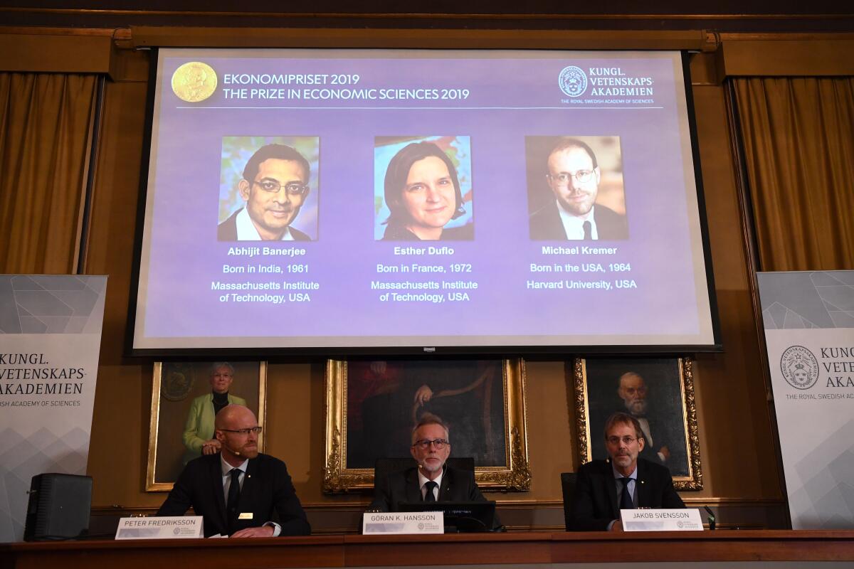 The 2019 Nobel Memorial Prize in economics winners are projected on a screen at the Royal Swedish Academy of Sciences in Stockholm on Monday. They are, from left on screen, Abhijit Banerjee, Esther Duflo and Michael Kremer.