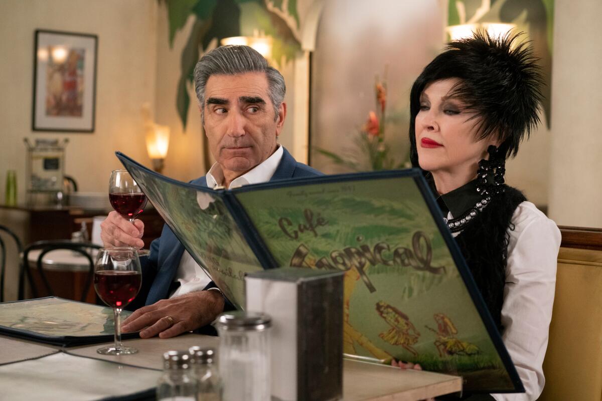 A man holding a glass of wine looks sideways at a woman who's perusing a large menu next to him in a restaurant booth.