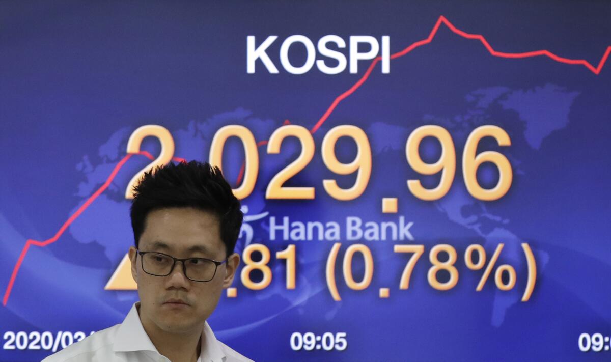 A currency trader in Seoul walks by a screen March 4 showing the Korea Composite Stock Price Index.