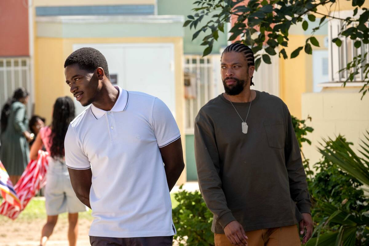 A man in a white polo shirt leans to the side and stands next to a man in a long-sleeve black shirt.