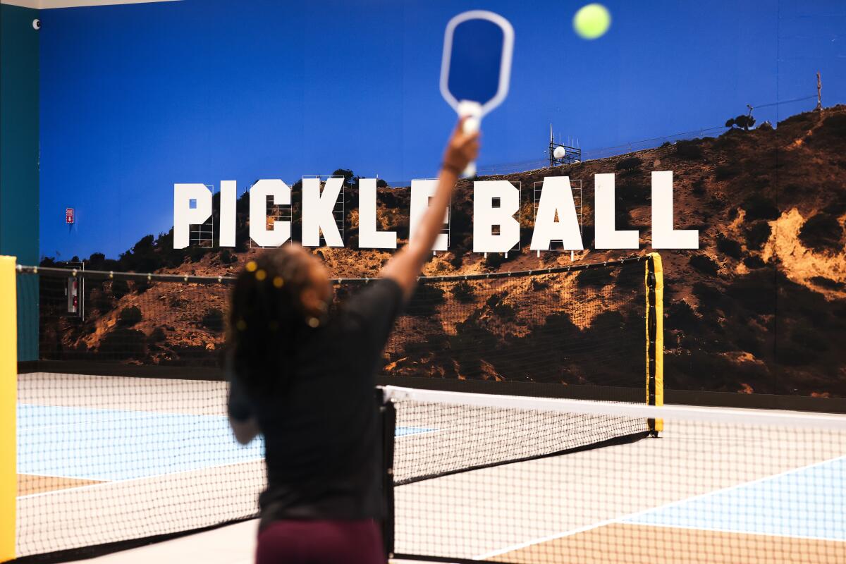 A woman plays on the pickleball court, which has a mural with the word Pickleball in the style of the Hollywood sign