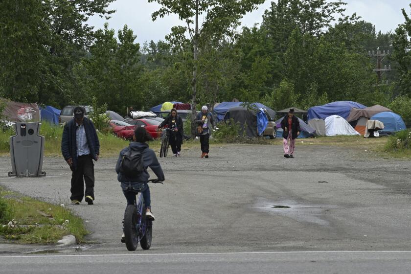 People walk towards East Third Avenue from a homeless encampment on Wednesday, June 21, 2023, in Anchorage, Alaska. An unfunded proposal by Anchorage’s mayor to pay for plane tickets to warmer climates for homeless people who would otherwise be forced to winter outside in the bitter cold has caused a stir in Alaska’s biggest city. If the program moves forward, people can choose to relocate to the Lower 48 or somewhere else in Alaska where it might be warmer or where they have relatives. (Bill Roth/Anchorage Daily News via AP)