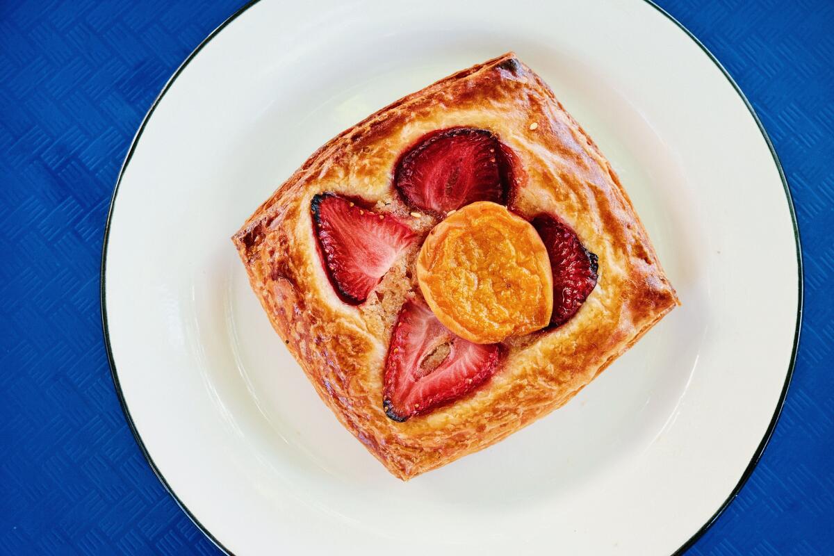 An overhead of a strawberry and apricot croissant danish on a bright blue tray from Baker's Bench bakery.