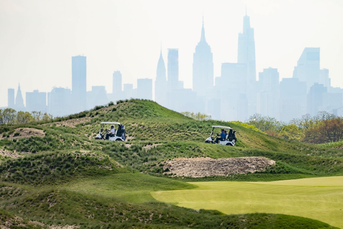 FILE - Patrons play the links as the Manhattan skyline looms in the distance at Trump Golf Links at Ferry Point in the Bronx borough of New York, May 4, 2021. Donald Trump's company can keep running a public golf course in the Bronx, a judge ruled Friday, April 8, 2022, saying New York City offered a baseless rationale for canceling the Trump Organization's contract to run the course after the insurrection at the U.S. Capitol in 2021. The ruling sends the matter back to the city "for further proceedings." It wasn't immediately clear what those might be; a request for comment was sent to city officials. (AP Photo/John Minchillo, File)