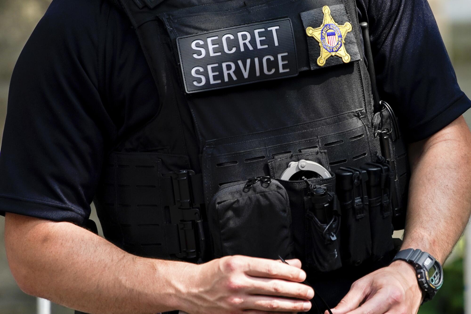 A close-up of a Secret Service agent in a black shirt and black vest.