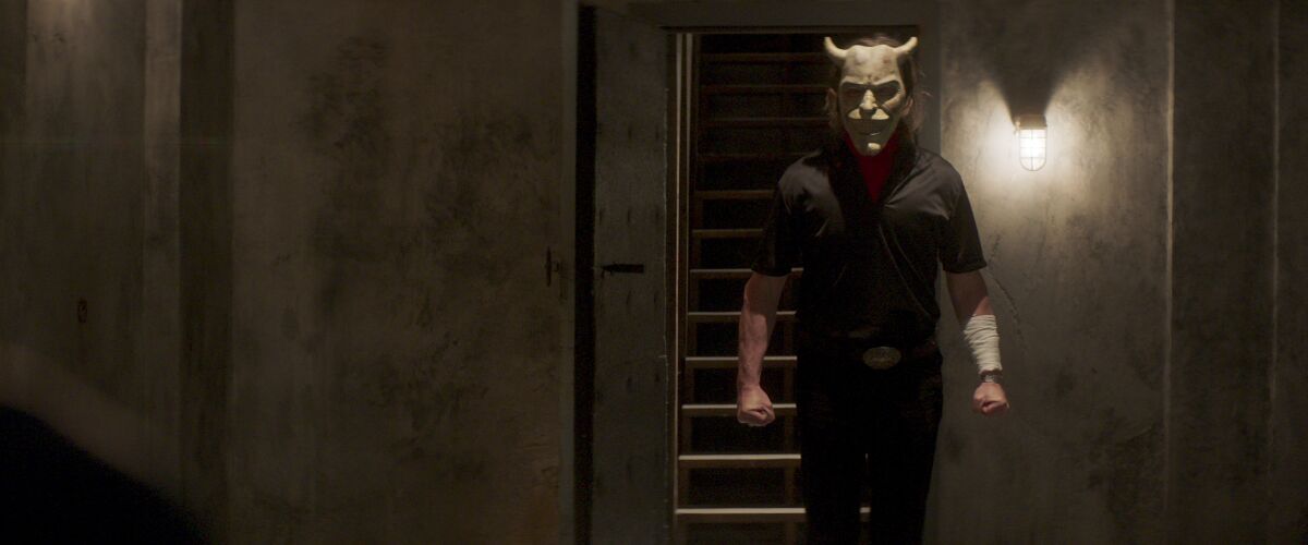 A man in a horned mask walks while clenching his fists