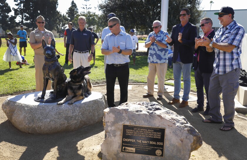 Trevor Maroshek, with his service/therapy dog Thor (son of Chopper), pose with the new memorial statues just after the unveiling of Imperial Beach's Military Service Dog Memorial Statue on Saturday at Veterans Park in Imperial Beach. On the stage from left to right are: Captain Tim Slentz, Commander Naval Base Coronado, Andrew Tefeslki , of the Naval Seal Foundation, IB council member Bobby Patton (behind Maroshek), former SD Mayor Jerry Sanders, Imperial Beach Mayor Dedina, Councilman Mark West and community member Jerry Quinn.
