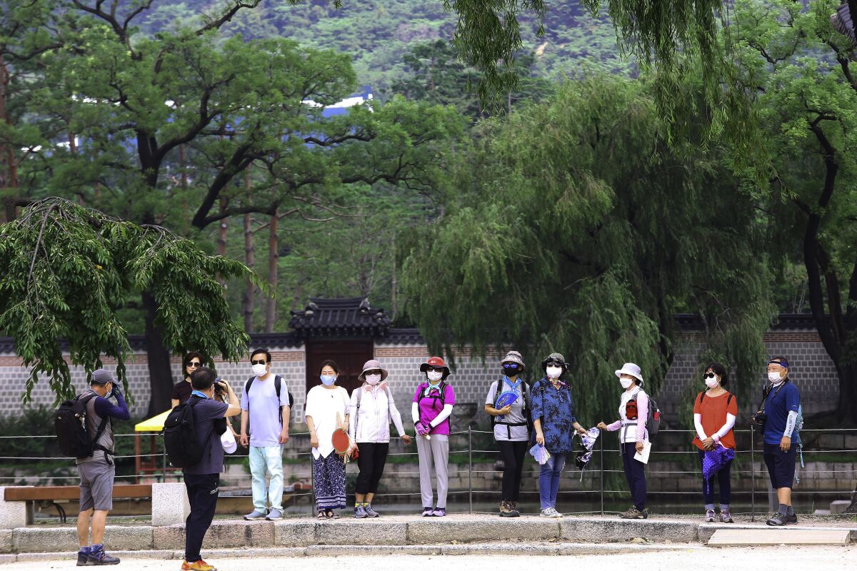 Visitors wearing face masks to help protect against the spread of the coronavirus pose to take pictures at the Gyeongbok Palace in Seoul, South Korea, Monday, Aug. 17, 2020. South Korea counted its fourth straight day of triple-digit increases in new coronavirus cases Monday as the government urged people to stay home and curb travel. (AP Photo/Ahn Young-joon)