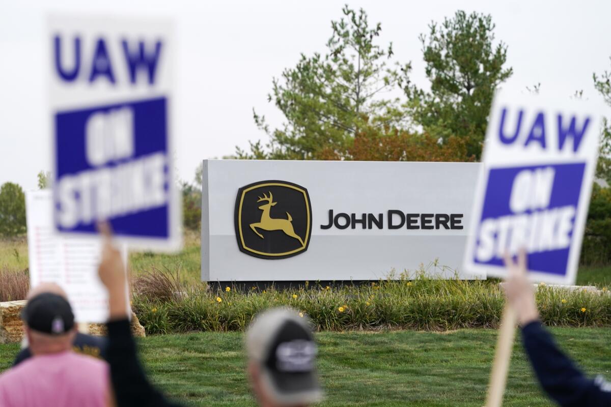 Picketers hold signs in front of a John Deere sign