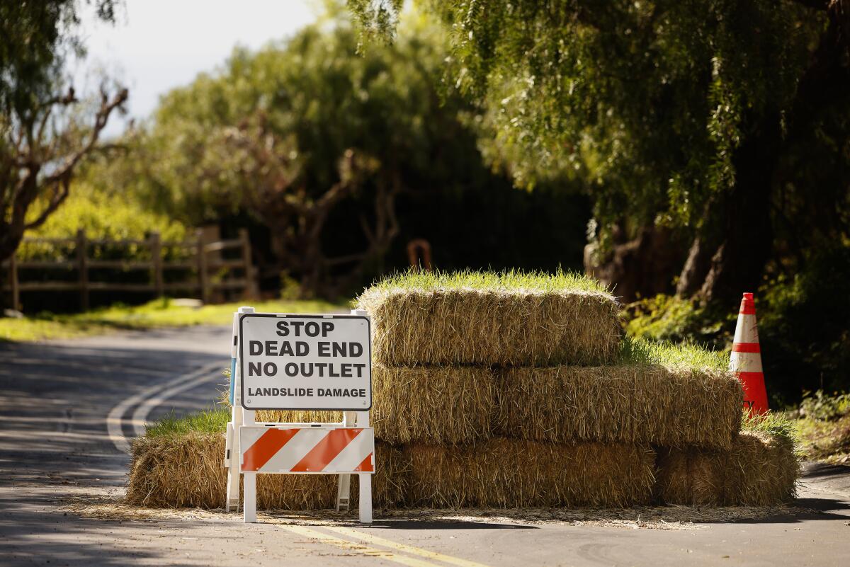 Bales of hay are set across a road. Next to them is a sign that says "Stop, dead end, no outlet."