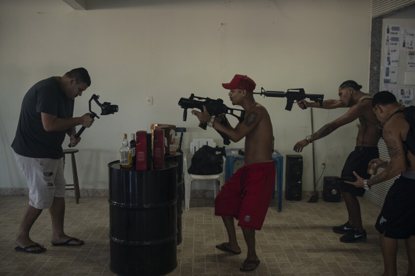 Trap de Cria artists Marcos Borges, known as "MbNaVoz," center, Pablo "PBSant," second right, and Fernando "Barbeirin," right, hold Airsoft guns as cameraman Clayton Oliver, left, records a music video for the song "Se Tem Glock" in the Jardim Catarina community in Sao Gonçalo, Rio de Janeiro state, Brazil, Sunday, April 11, 2021. Trap de Cria has a lyrical flow over synthesized drums, and is comparable to U.S. gangsta rap in speaking to the day-to-day struggles of hardscrabble hoods while depicting gang life. (AP Photo/Felipe Dana)